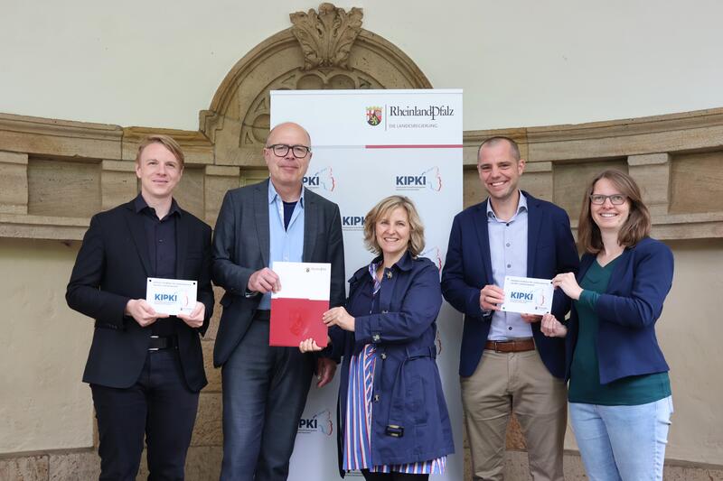 Fr&ouml;hliche Gesichter in Landau: Klimaschutzministerin Katrin Eder (Mitte) &uuml;berreicht den KIPKI-F&ouml;rderbescheid an Oberb&uuml;rgermeister Dominik Gei&szlig;ler (2.v.l.) und B&uuml;rgermeister Lukas Hartmann (links) im Beisein der Landtagsabgeordneten Dr. Lea Heidbreder und 