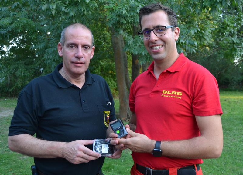 Der Landauer Stadtfeuerwehrinspekteur Dirk Hargesheimer (l.) und Simon Nichterlein, Technischer Leiter der DLRG Ortsgruppe Landau, bei der &Uuml;bergabe der digitalen Funkmeldeempf&auml;nger an das DLRG. 