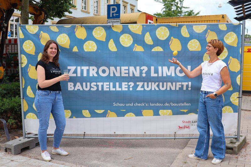Nina Ziegler (l.) und Carolin Bader vom Tourismusb&uuml;ro vor einem der Baustellenbanner - in der Waffenstra&szlig;e. 