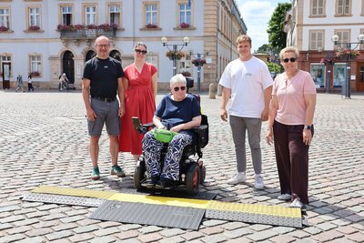 Bild vergr&ouml;&szlig;ern: Von links: Maik Leidner, Beauftragter f&uuml;r die Belange von Menschen mit Behinderung der Stadt Landau, Nina Ziegler, Gesch&auml;ftsf&uuml;hrerin der StadtLeben Landau in der Pfalz GmbH, Gertrud Gerdon vom Kommunalen Beirat f&uuml;r die Teilhabe von Menschen mit Behinderungen, Niklas Frank und Sonja Brunner-Hagedorn, Marktmeister und Marktmeisterin der Stadt Landau, freuen sich &uuml;ber die neuen barrierefreien Kabelbr&uuml;cken auf dem Landauer Wochenmarkt.