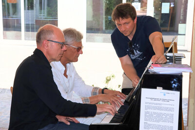 Bild vergr&ouml;&szlig;ern: Oberb&uuml;rgermeister Dominik Gei&szlig;ler und K&uuml;nstler Thomas Sedlmayr, unterst&uuml;tzt durch Adrian Rinck, Leiter der Kreismusikschule S&uuml;dliche Weinstra&szlig;e, mit der &raquo;Jazz Suite for Piano Duet&laquo; von Mike Cornick.