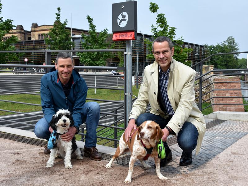 B&uuml;rgermeister Dr. Maximilian Ingenthron (r.) und Ralf Bernhard vom Stadtbauamt mit vierbeiniger Begleitung an einem der neuen Spender f&uuml;r Hundekotbeutel entlang der Queichpromenade. 