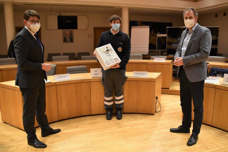 Symbolische Geste: OB Hirsch (links) und Landrat Seefeldt (rechts) &uuml;berreichen Kreisbereitschaftsleiter Marco Nau eine Thomas-Nast-Nikolausbox zum Dank f&uuml;r seinen Einsatz an der Teststation.