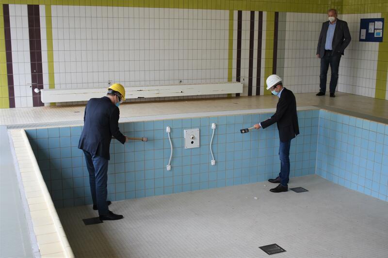 Es kann losgehen: Landrat Dietmar Seefeldt (links) und Landaus B&uuml;rgermeister Dr. Maximilian Ingenthron beim ersten Hammerschlag f&uuml;r die Sanierung des Bewegungsbades in der Paul-Moor-Schule. 