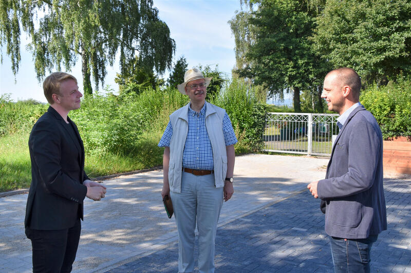 Beigeordneter Lukas Hartmann (links) zusammen mit dem Leiter der st&auml;dtischen Friedhofsverwaltung Gerhard Blumer und Ortsvorsteher Florian Maier (rechts) auf dem frisch befestigten Parkplatz vor dem Dammheimer Friedhof. 